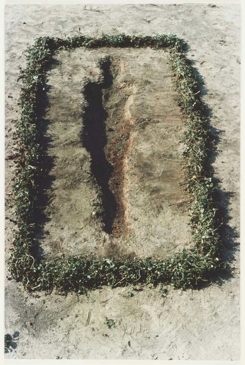 A photograph of a human silhouette that has been dug out on dry ground framed by a rectangle of grass.